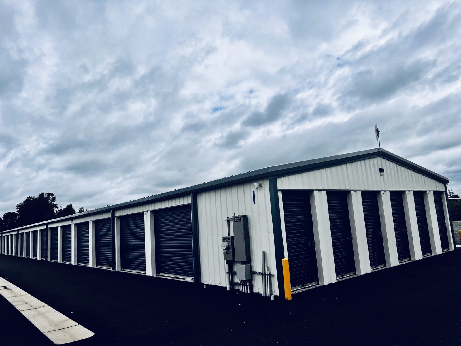 Row of steel self-storage units with dark roll-up doors under a dramatic sky