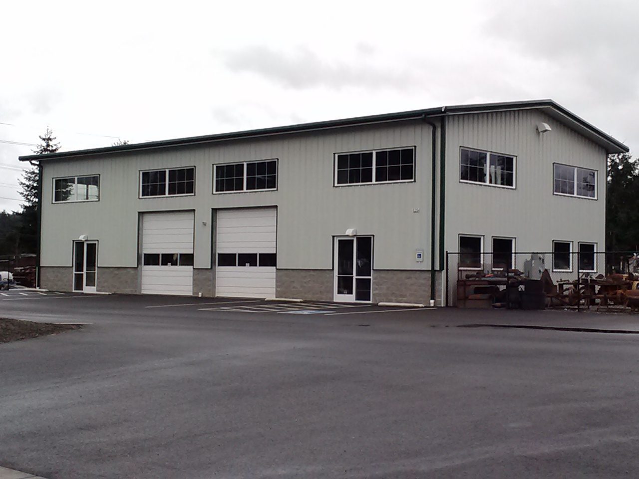 Two-story steel shop building with overhead doors and a fenced equipment yard